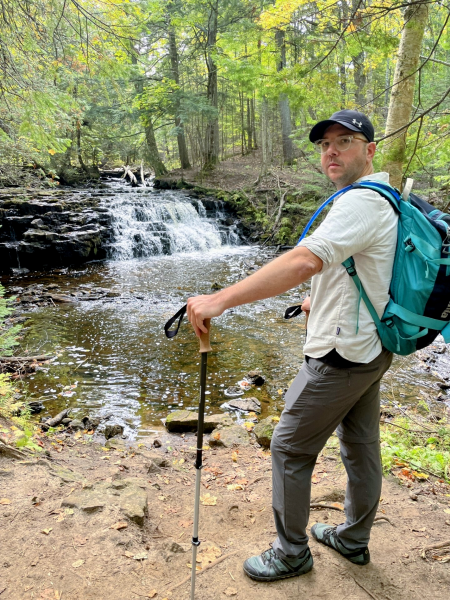 Phil C-B on a hike, stopped in front of a waterfall in the woods.